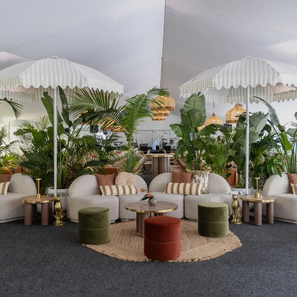 Common lounge area with a cream modular, coffee table, umbrellas, arden ottomans and greenery