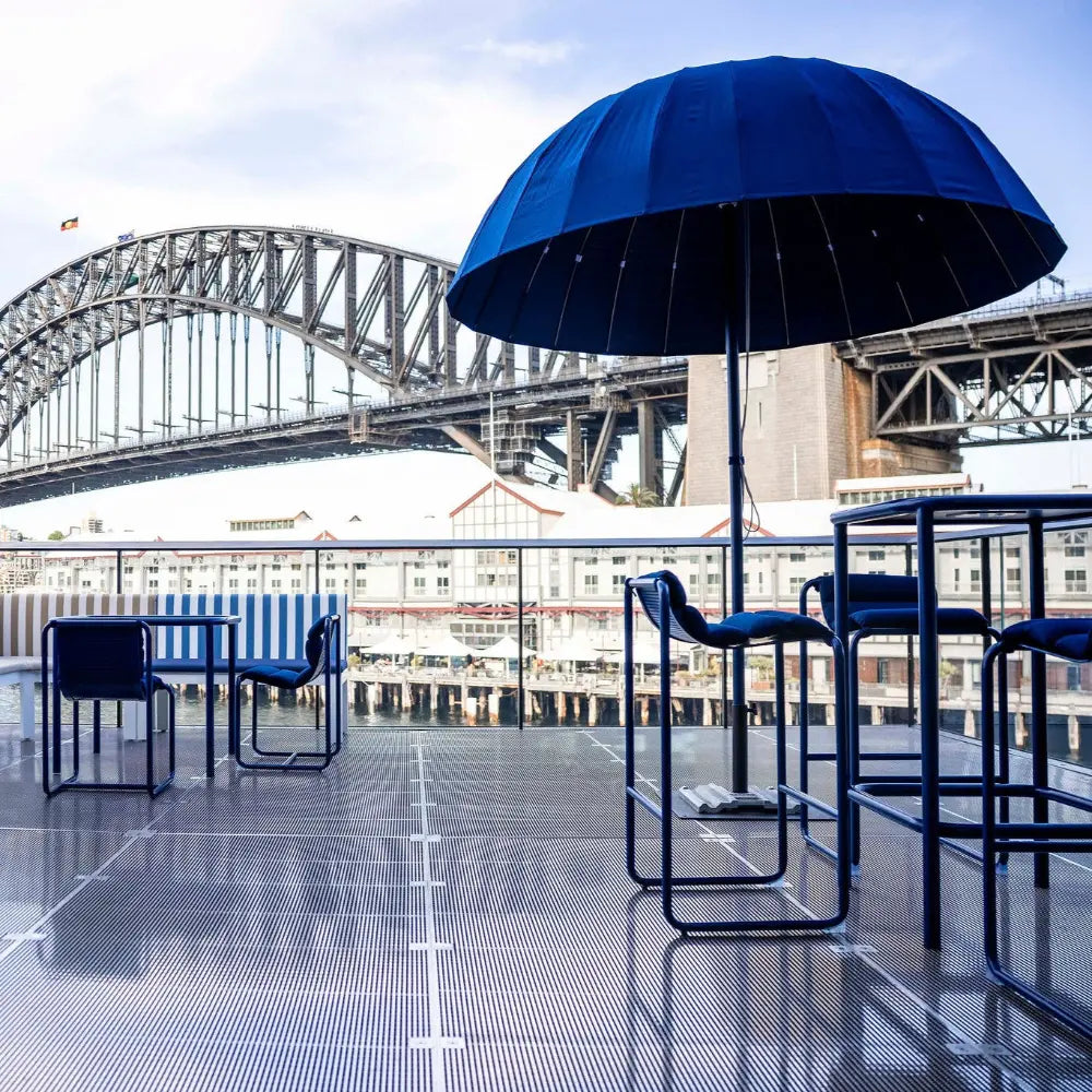 Balcony setup with bar stools and tables, lounges and umbrellas with the sydney harbor bridge in the background