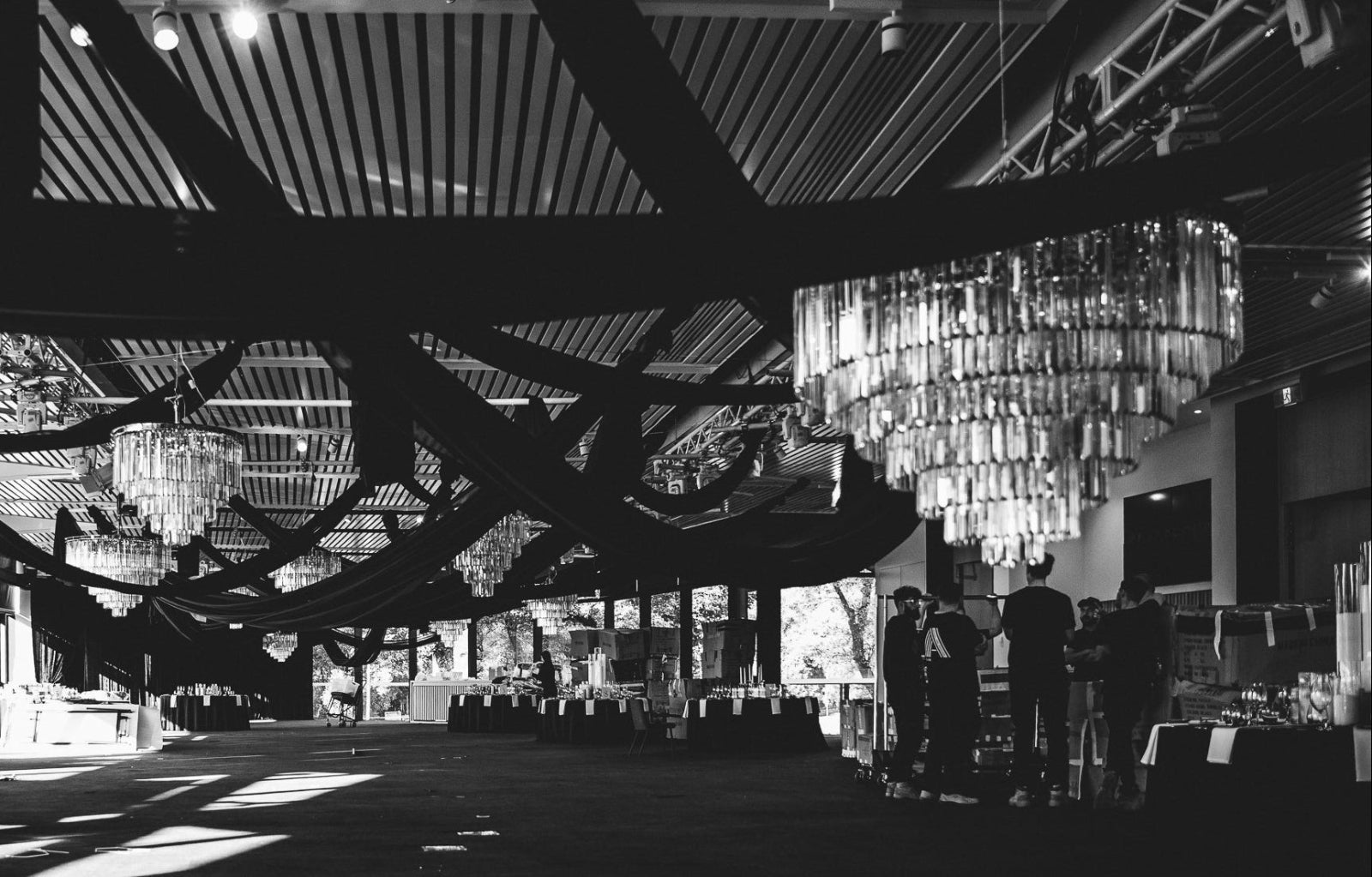Large indoor space with high ceilings, chandeliers, and people standing around.