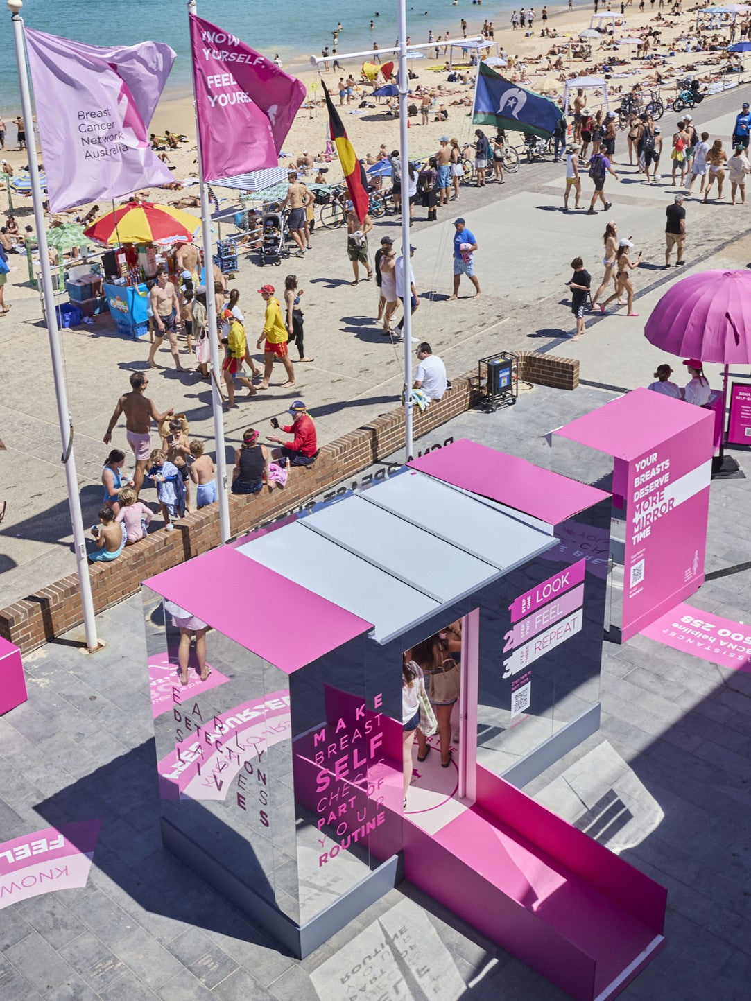 Pink mirrored booth on a beach with people and flags in the background