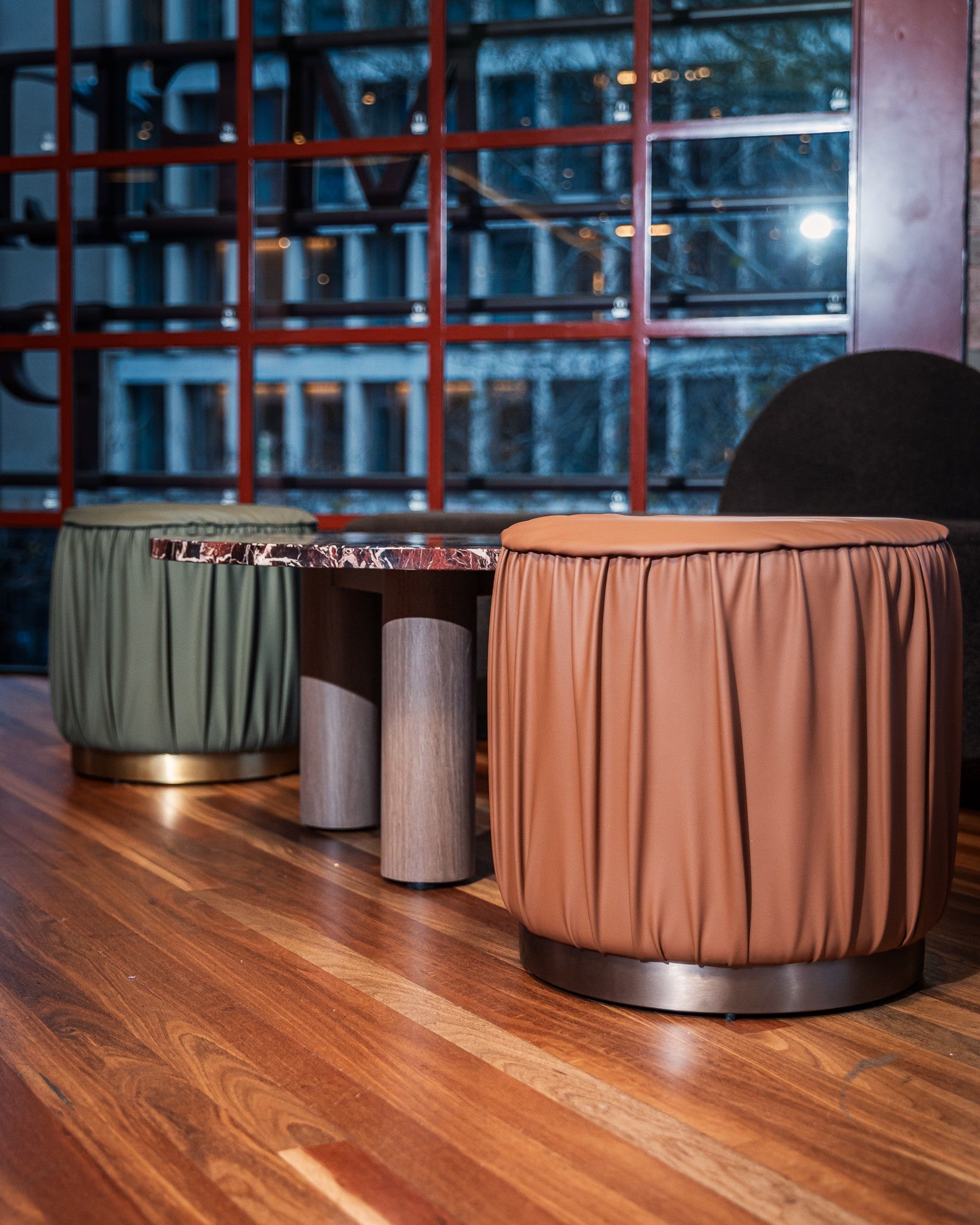 Three cylindrical stools with fabric covers on a wooden floor, with a reflective surface in the background.