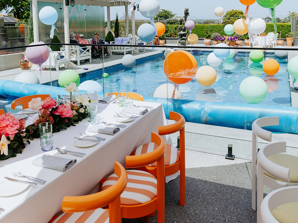 Outdoor pool party setup with colorful balloons, tables, and chairs by a pool.