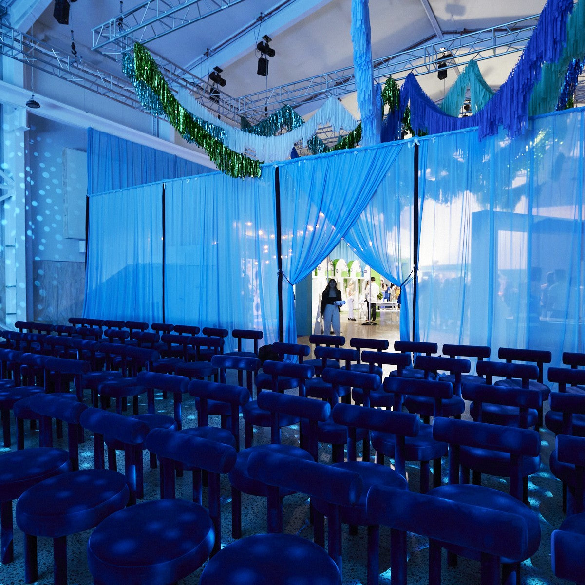Blue draped room with rows of chairs, set up for an event. Featuring our Totem Chairs.