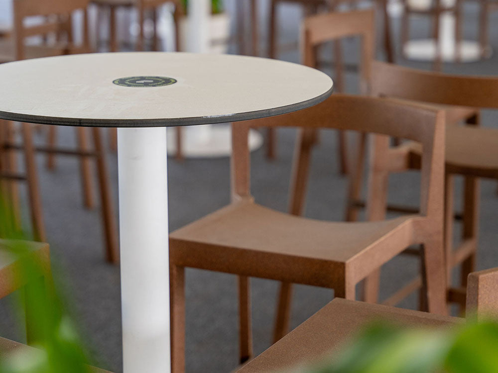 Round table with a white base in an indoor setting with chairs and plants.