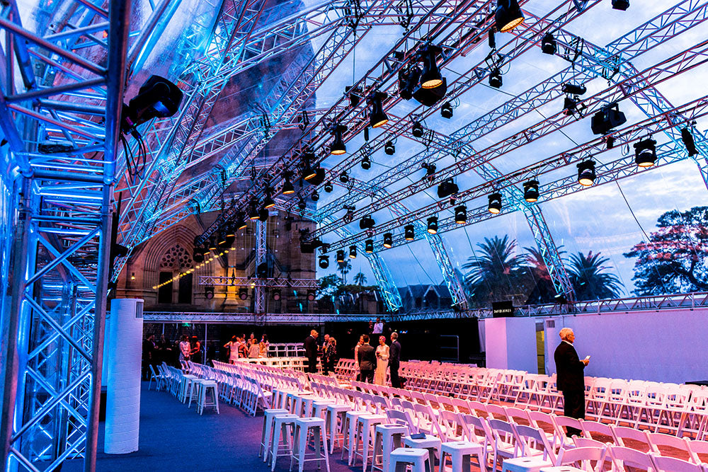 Large indoor event space with stage and audience seating, illuminated by blue lights. For Melbourne Fashion Festival