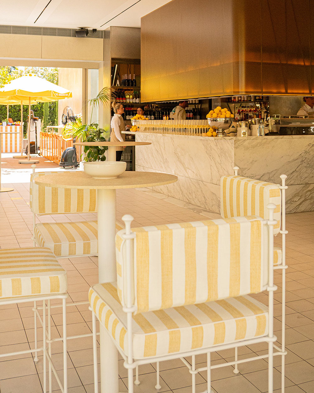 Outdoor cafe with yellow and white striped chairs and tables, and a bar in the background.