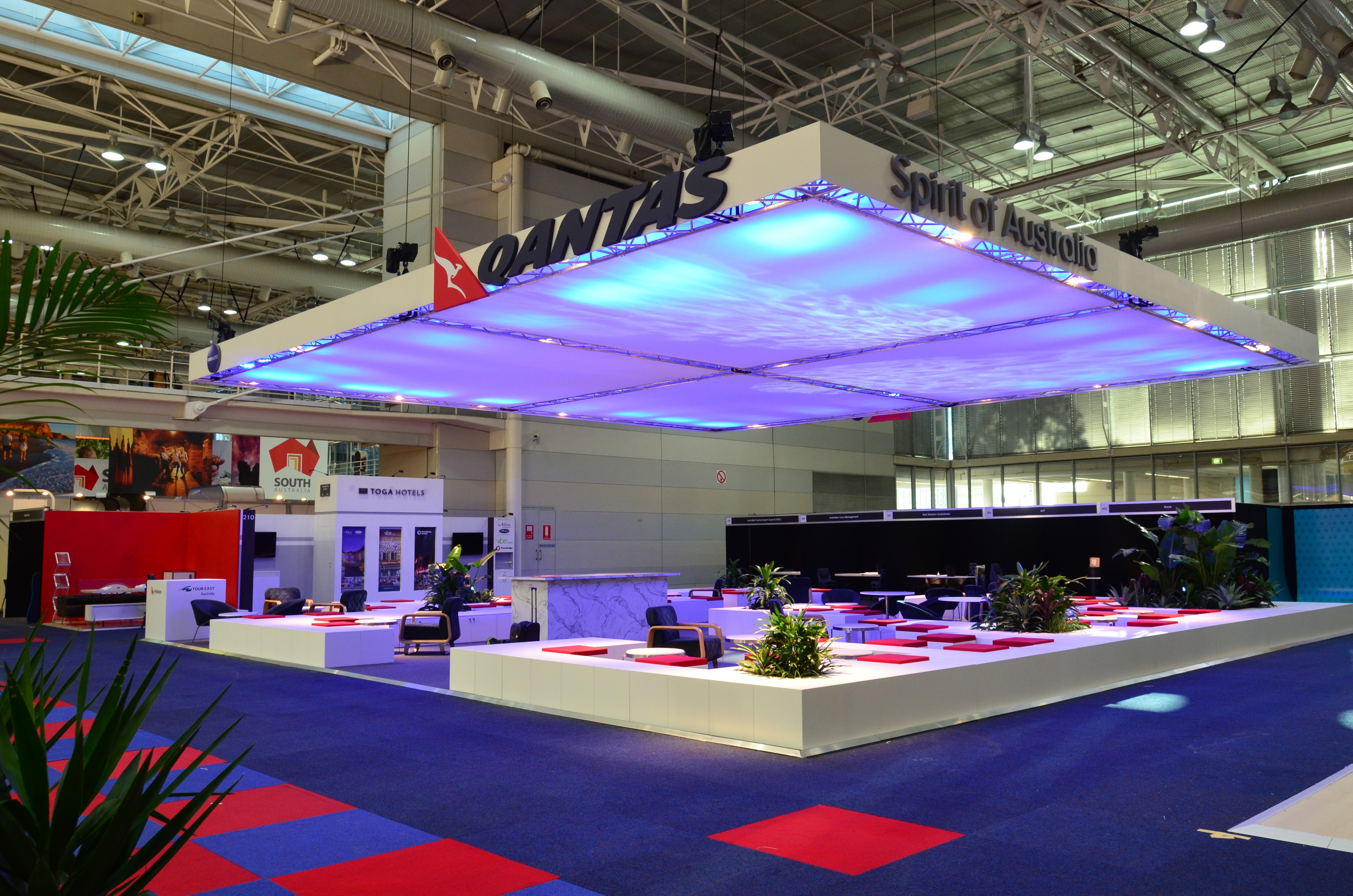 Qantas booth at an exhibition with a large sign and colorful ceiling design.