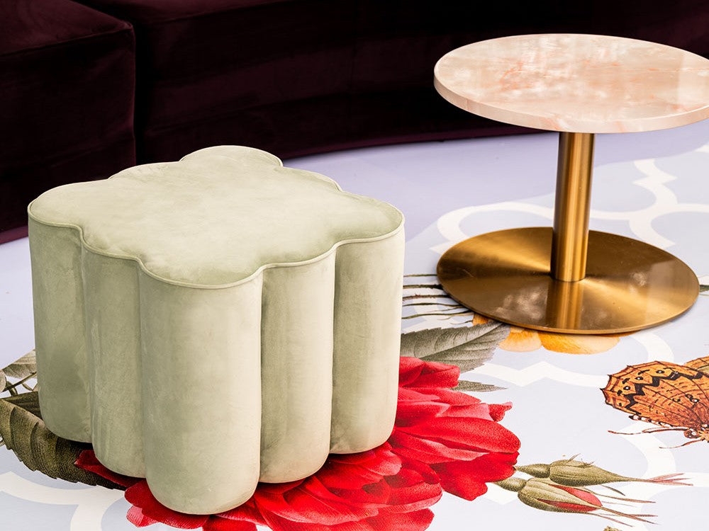 Decorative beige ottoman with a gold side table in the background