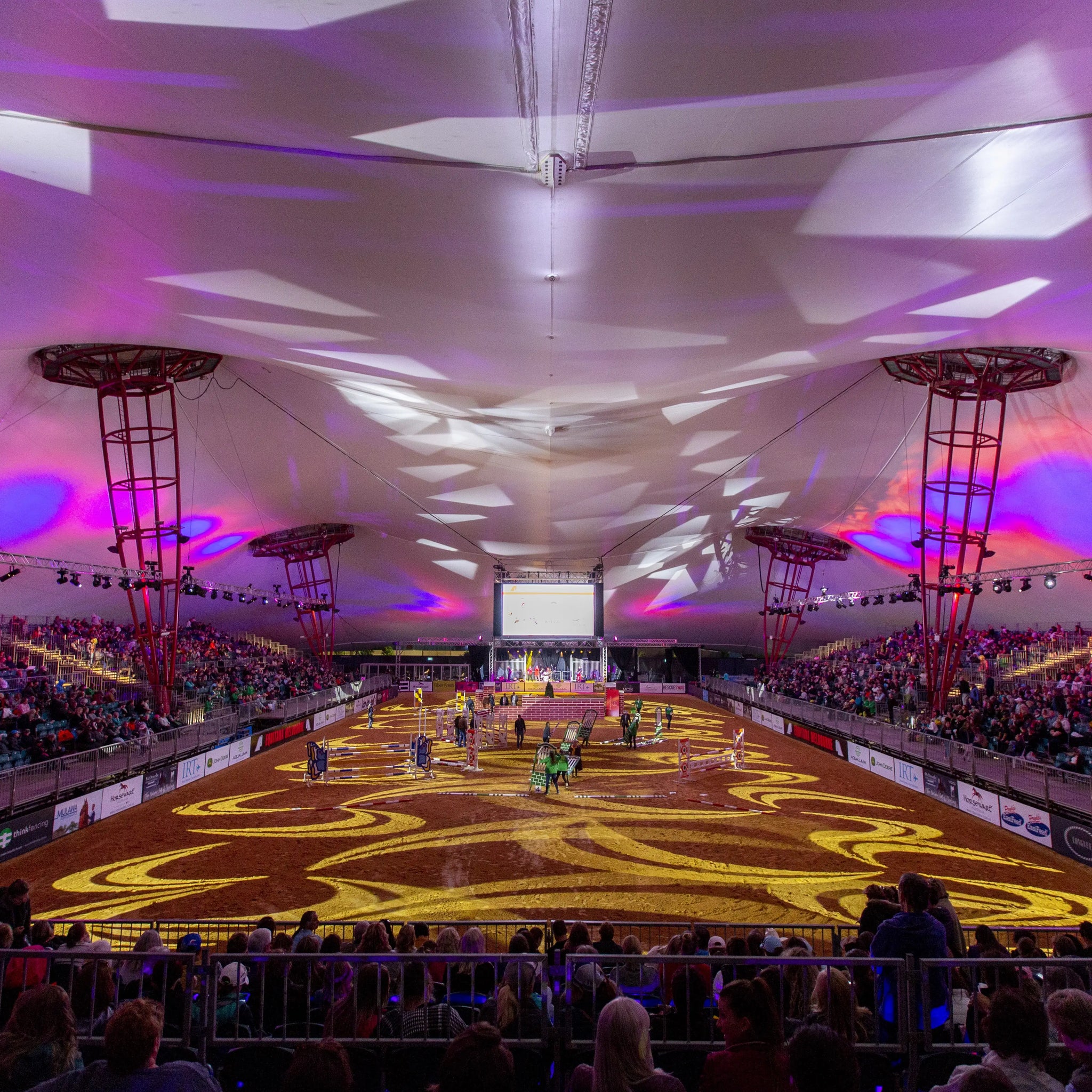 Indoor equestrian arena with a large crowd and colorful lighting