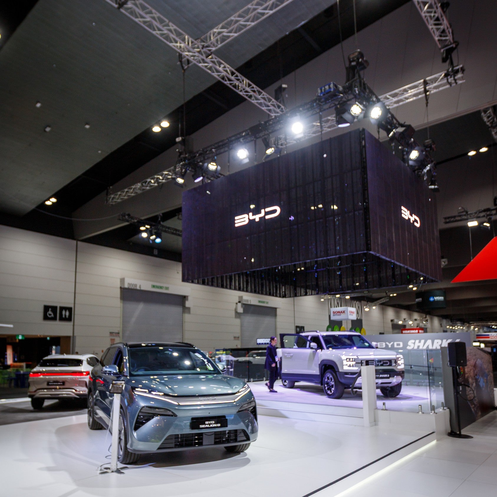 BYD vehicles on display at an indoor event with a large BYD logo overhead.