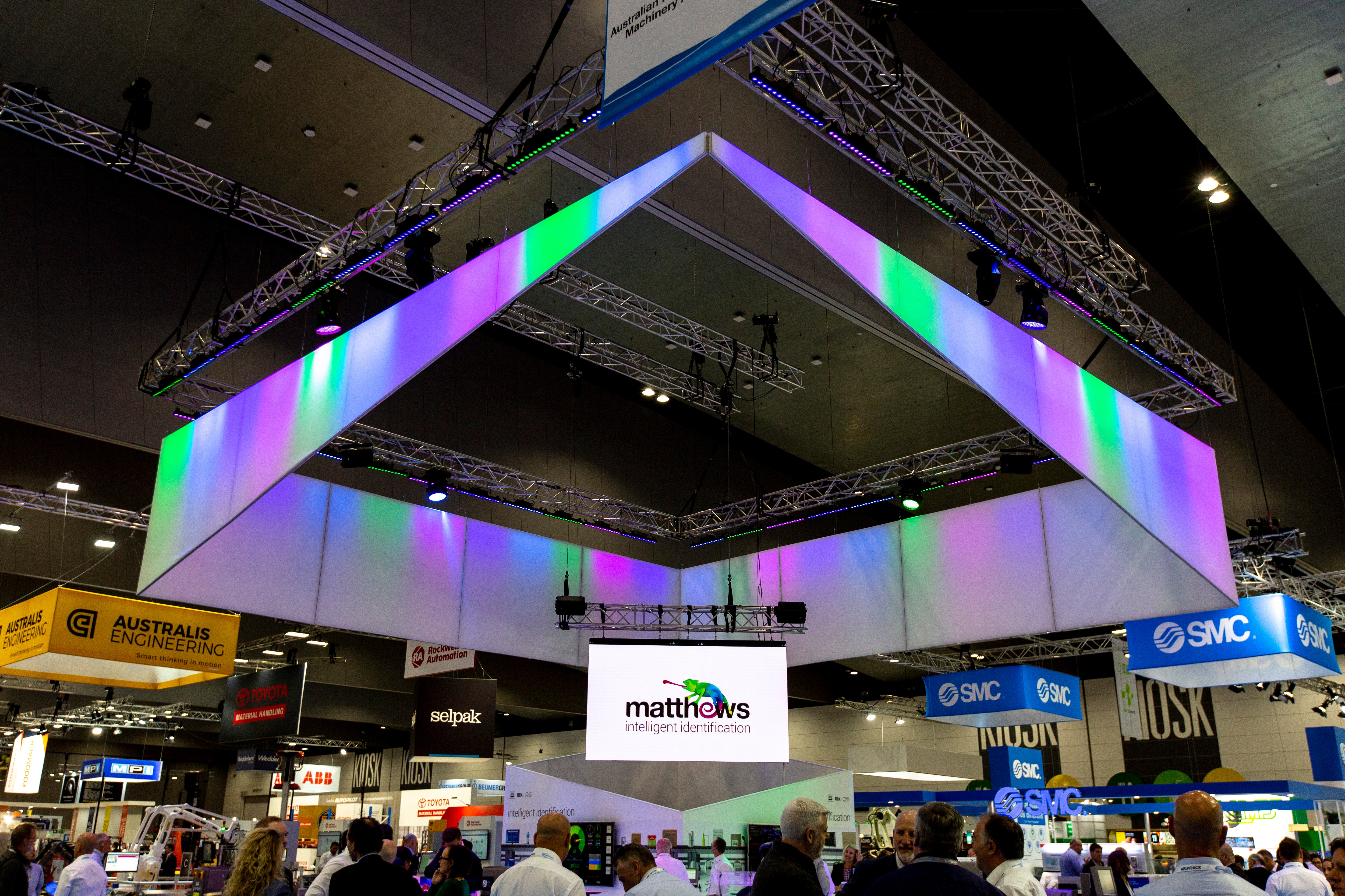 Exhibition hall with colorful ceiling design and various brand logos.