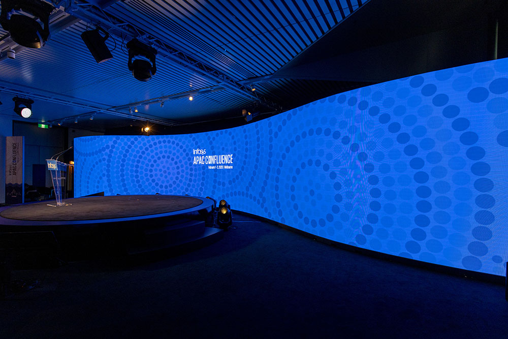 Stage with a large blue screen displaying 'APAC Confluence' in a darkened room.