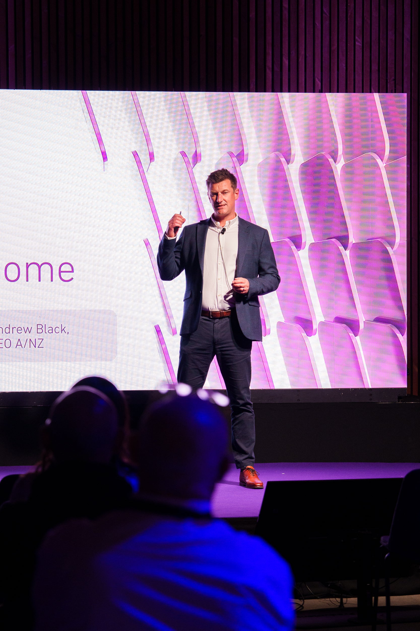 Man giving a presentation on a stage with a large screen displaying text in the background