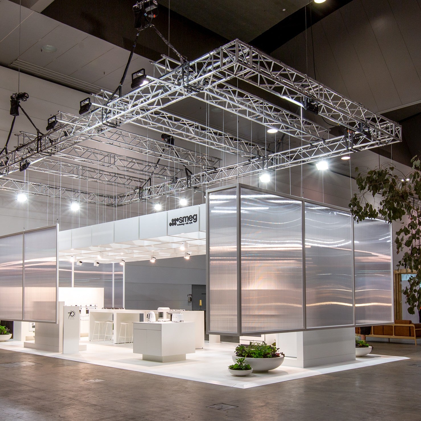 Modern trade show booth with glass walls and branding on a large indoor exhibition floor.