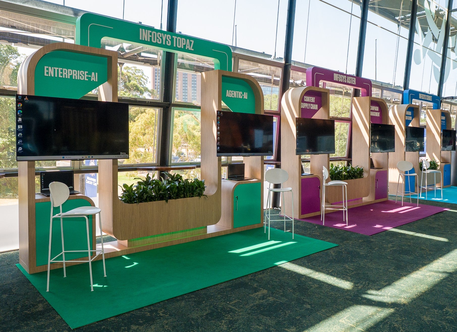 Infosys exhibition stand with multiple monitors and chairs in a bright indoor setting.