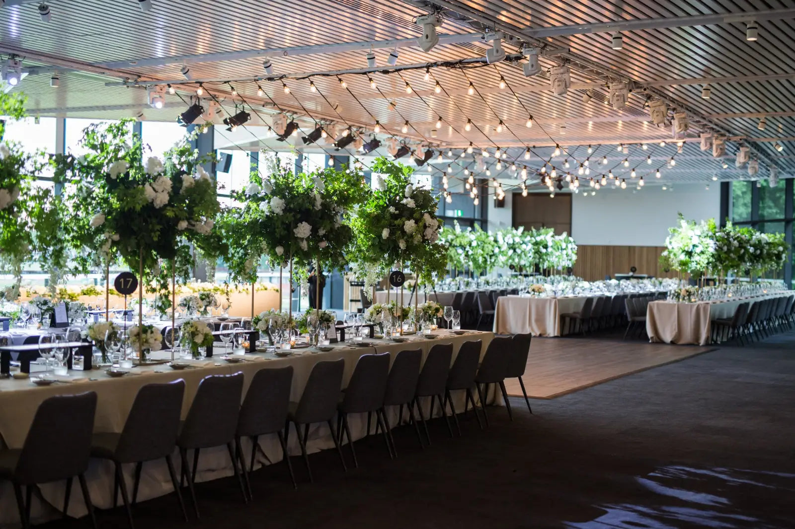 Dining room with tables set for a formal event, featuring tall glass vases with decorative elements.