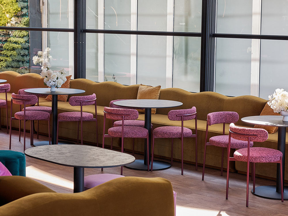 Modern interior with brown curved sofa, round tables, and pink chairs.