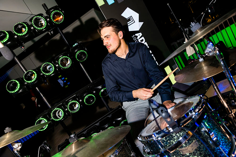 Man playing drums in a studio with drum equipment and green lights in the background at an Adelaide event