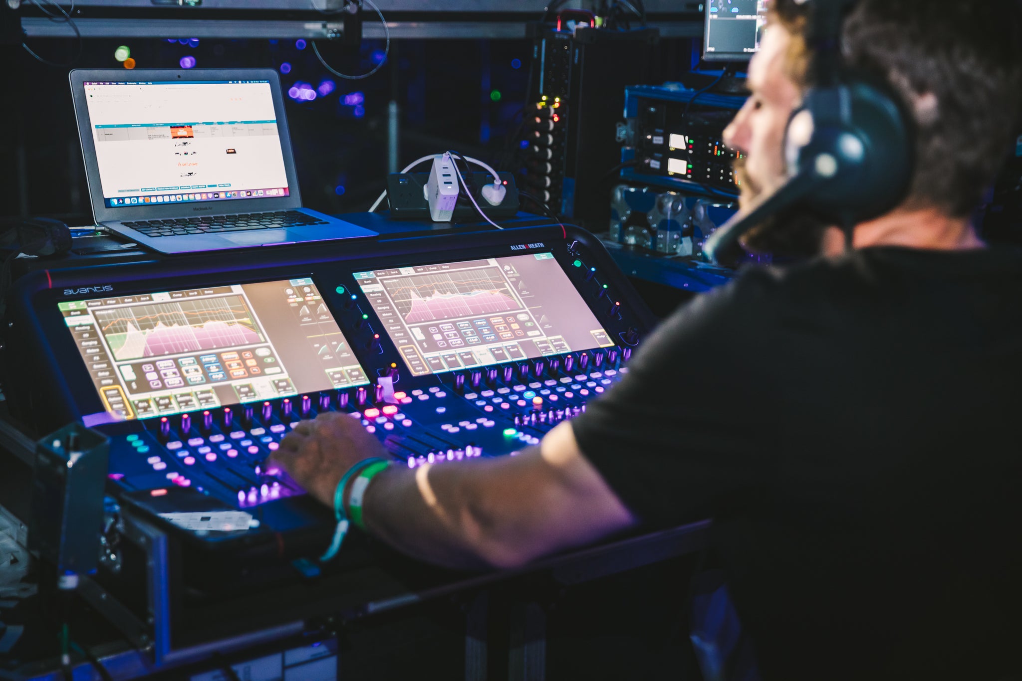 Harry the Hirer Productions operator operating audio mixing console with multiple screens in a control room setting.