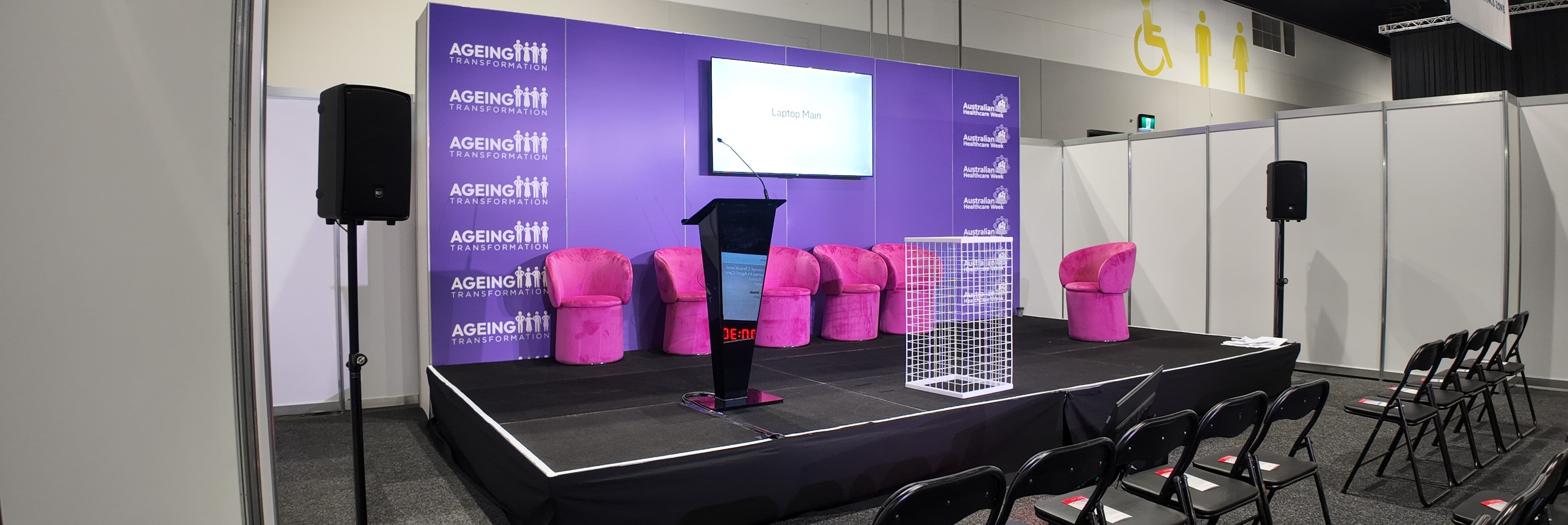 Stage setup with speakers, chairs, and a screen with branding.
