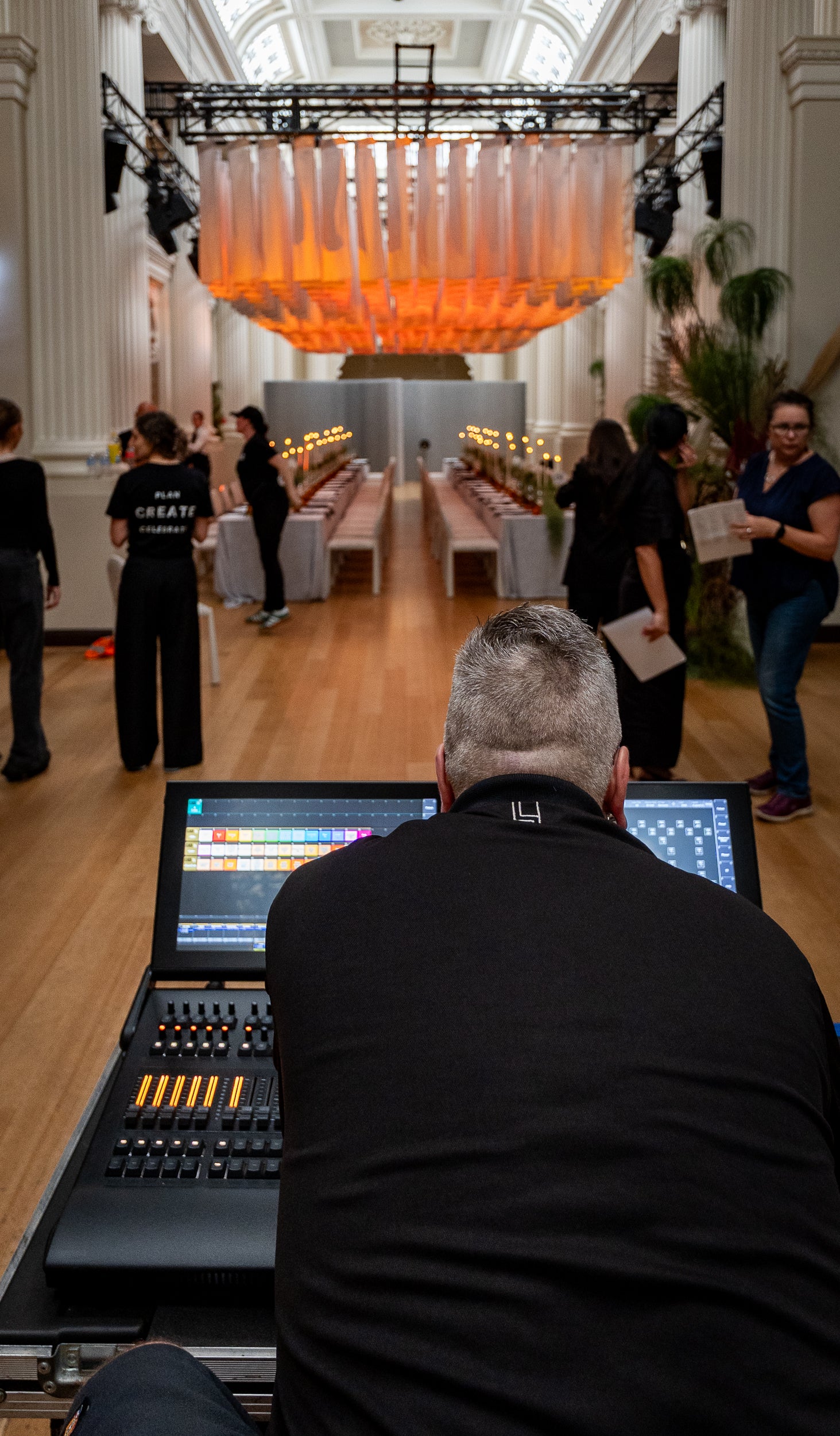 Person operating audio-visual equipment in a large indoor venue with people and tables in the background.