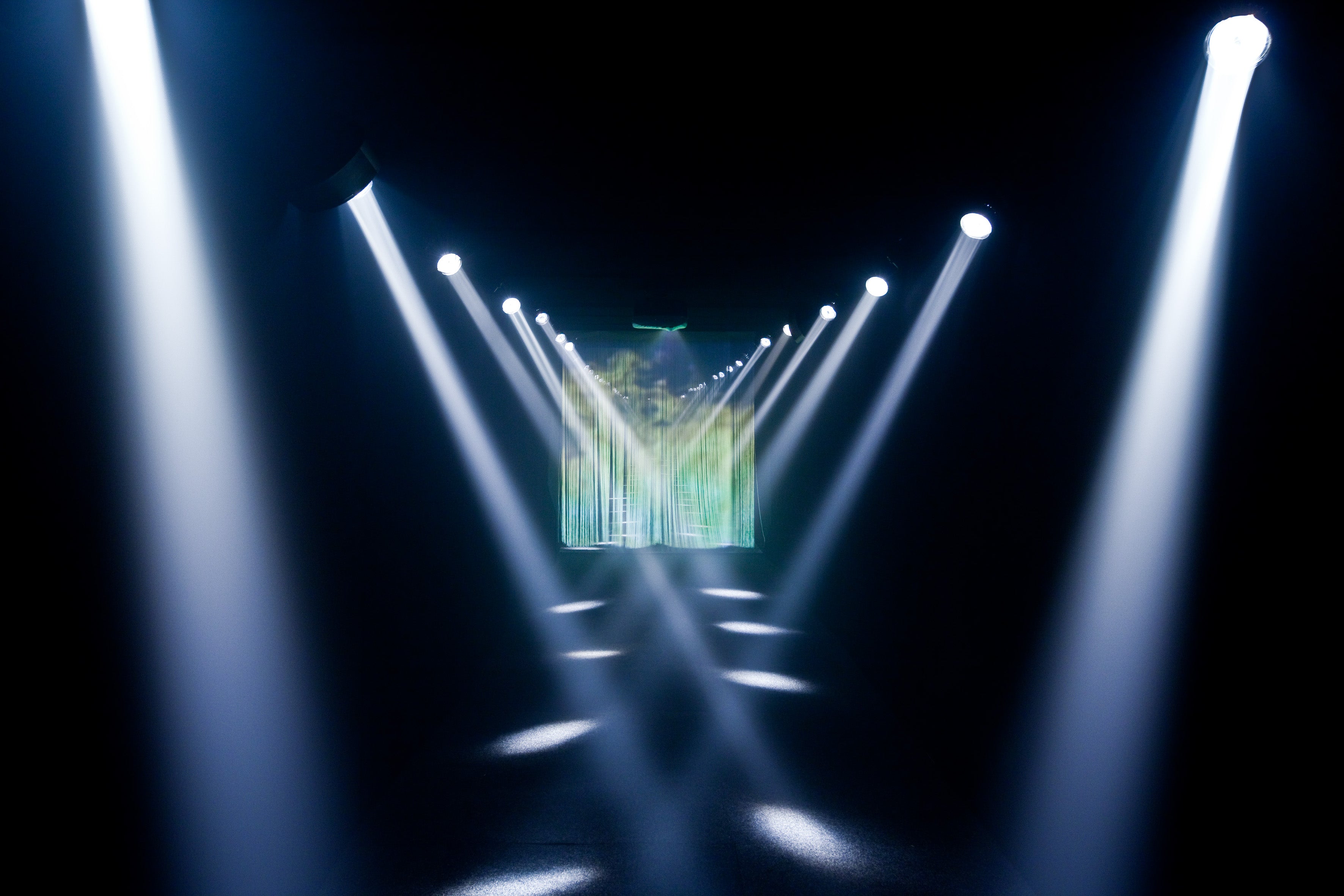 Stage lights converging towards a screen displaying a natural landscape.