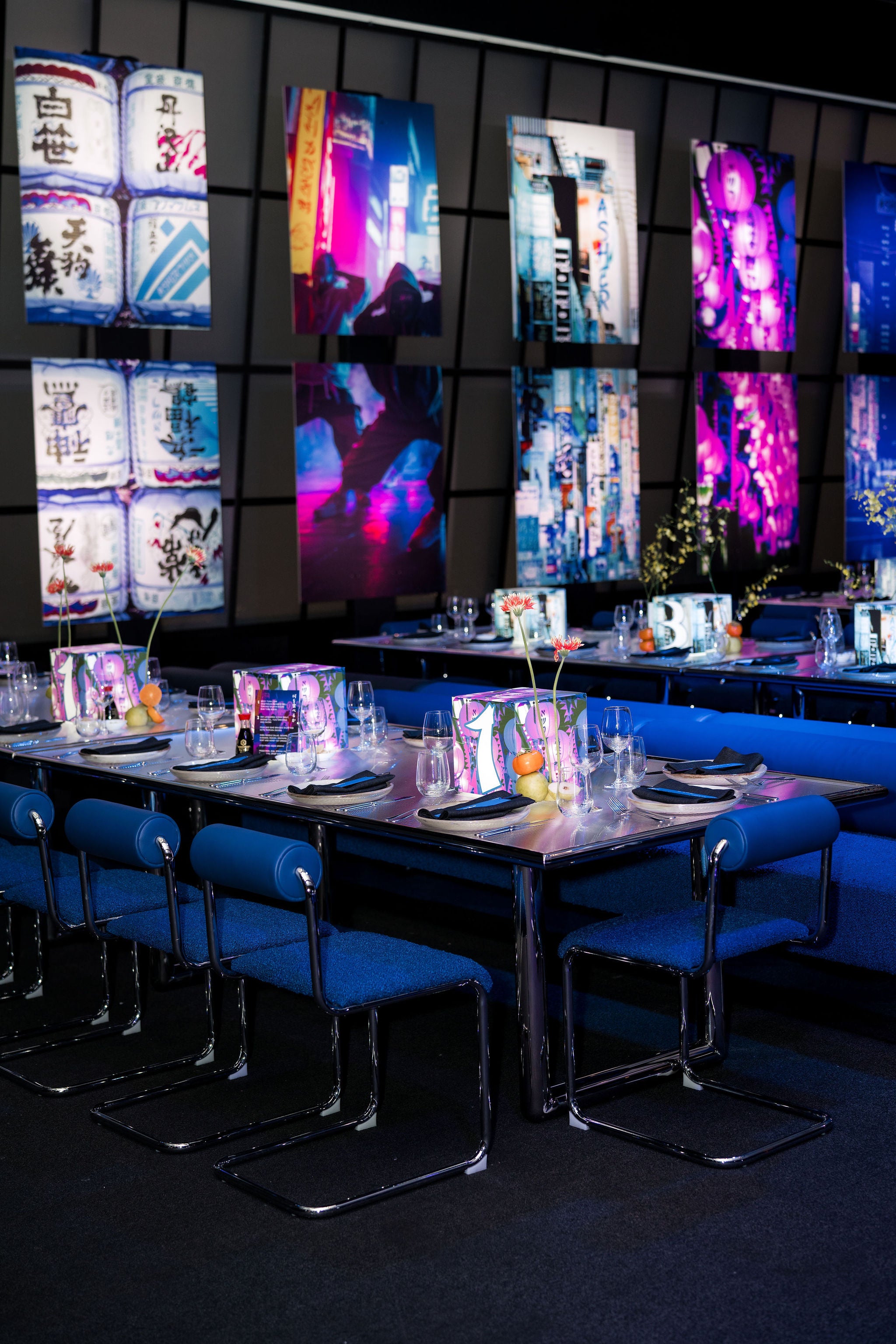 Modern restaurant interior with blue chairs and tables, colorful wall art, and a dark floor.