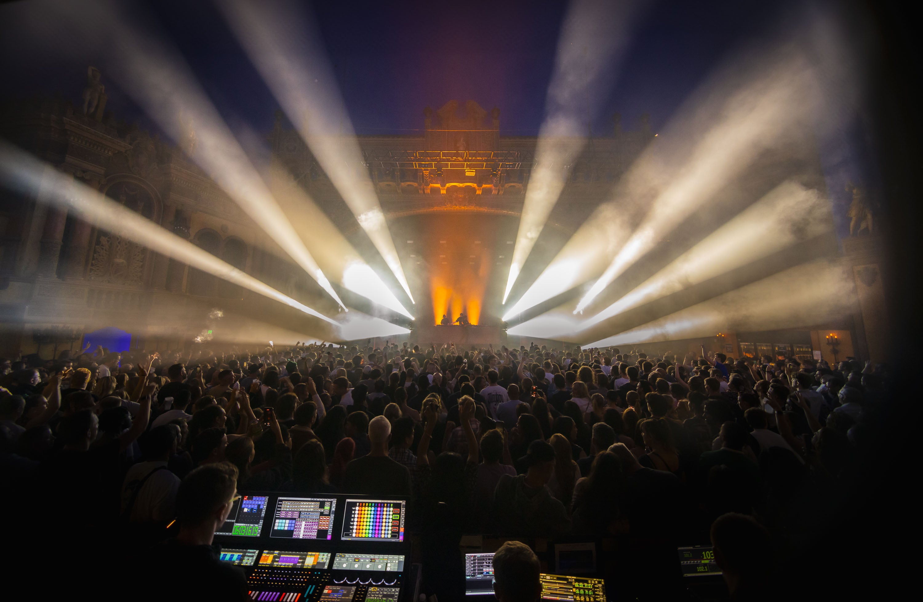 Large indoor event with stage lights and a crowd, possibly a concert or festival.