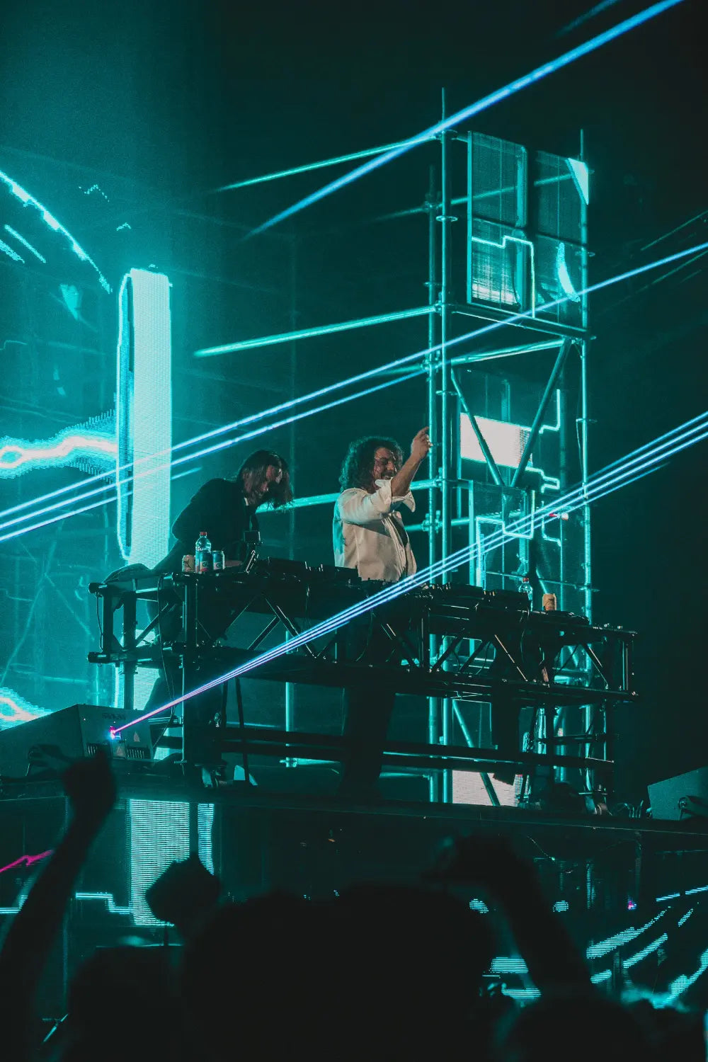 Two DJs on a stage with laser lights at a concert.