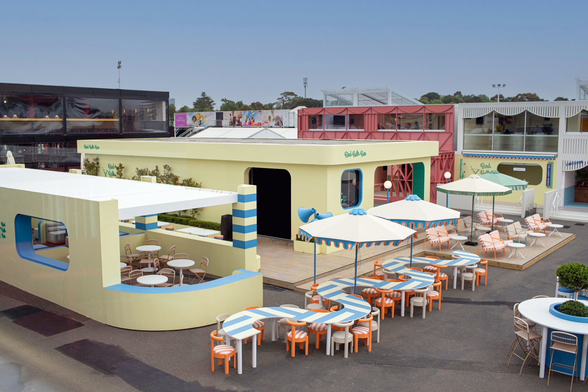 Outdoor seating area with tables, chairs, and umbrellas in a colorful building setting at Melbourne Spring Racing Carnival