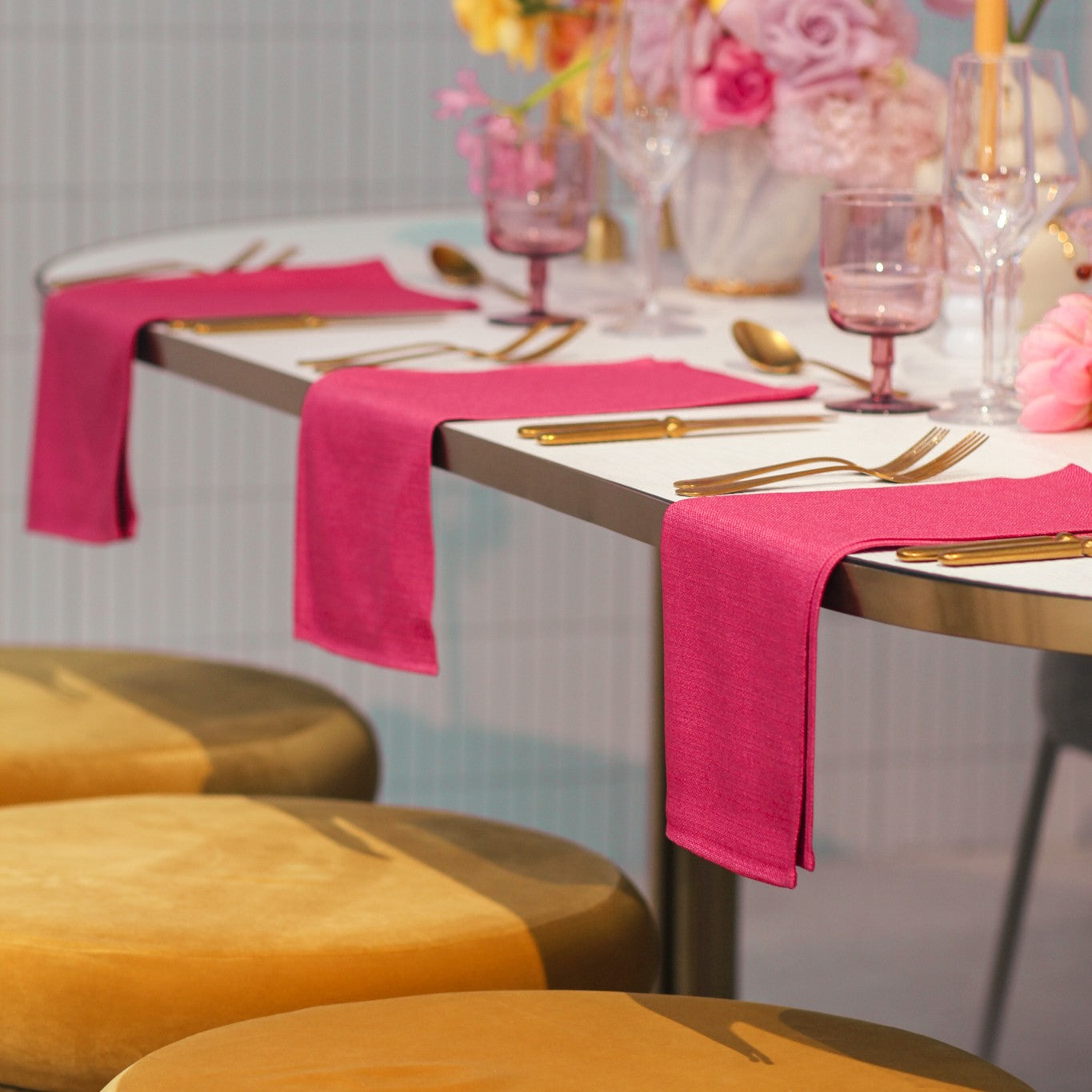 Dining table set with pink napkins, gold cutlery, and floral centerpieces.