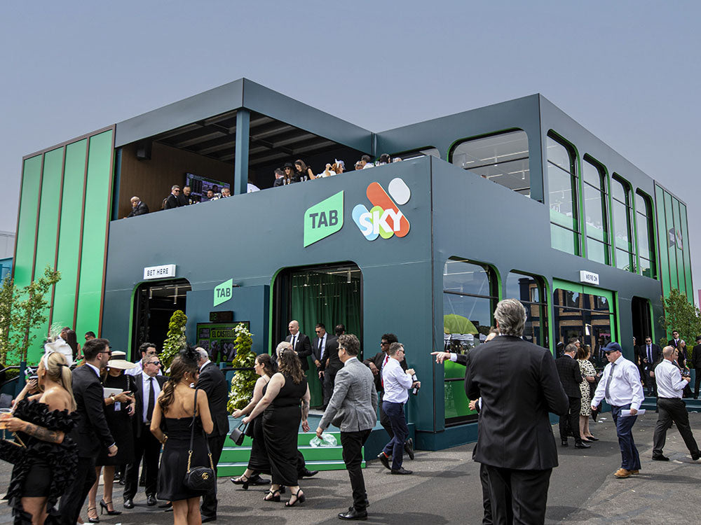 Modern building with 'TAB' branding, people gathered around, and a clear sky.