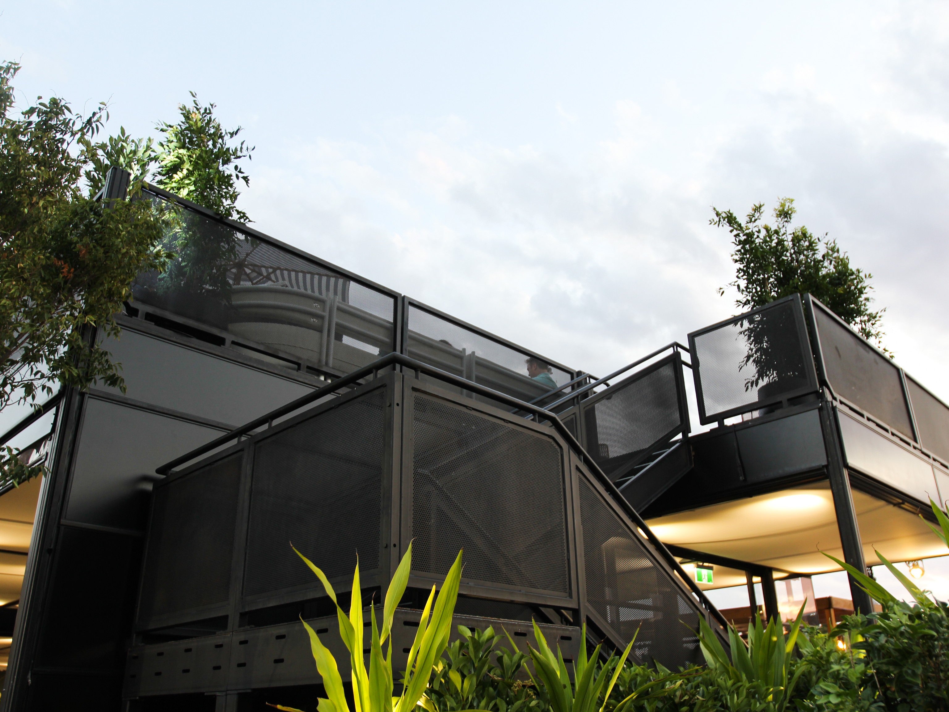Marquee structure with glass panels and metal frames, surrounded by greenery.