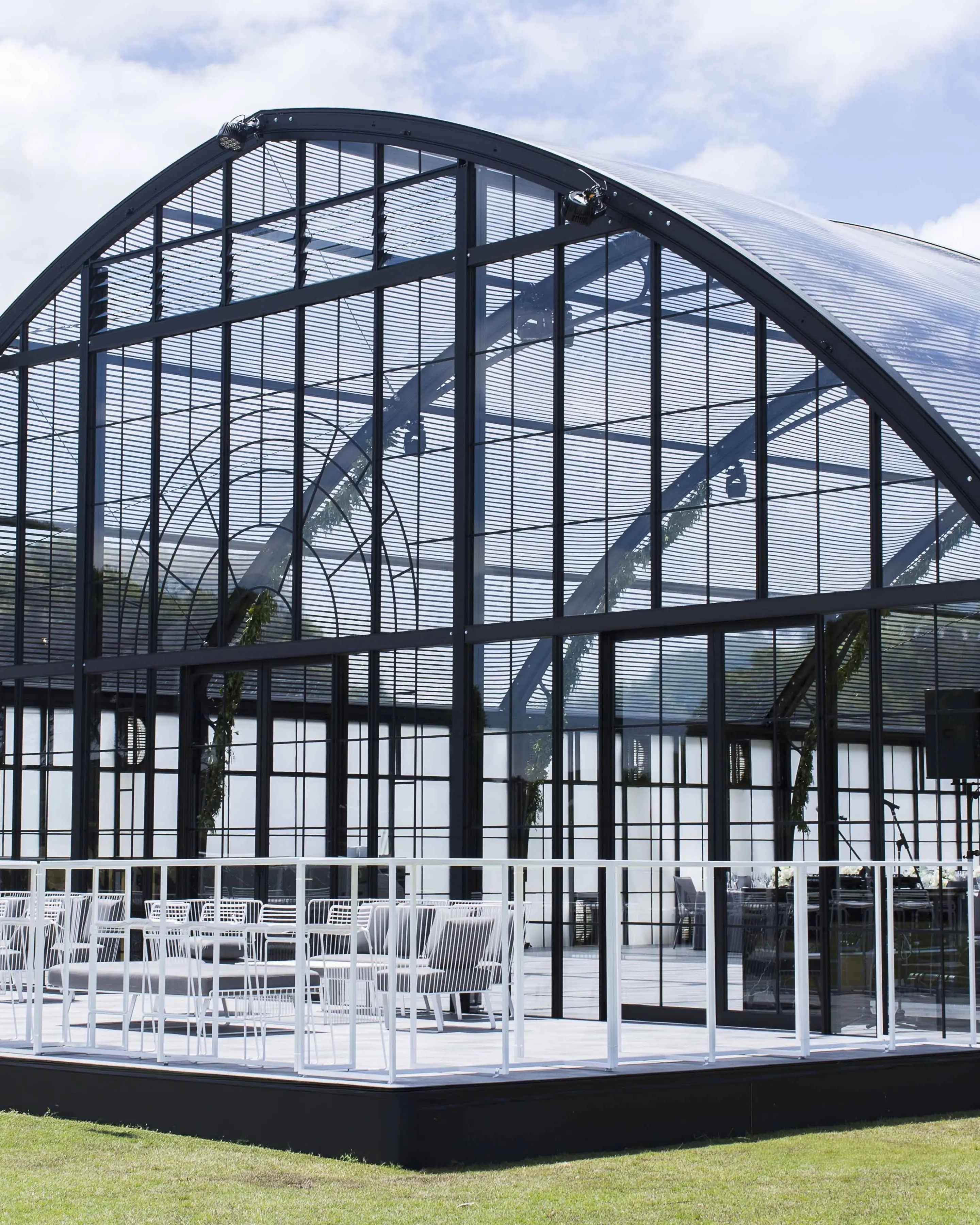 Large glass Atrium structure with arched roof and white chairs outside for a private wedding