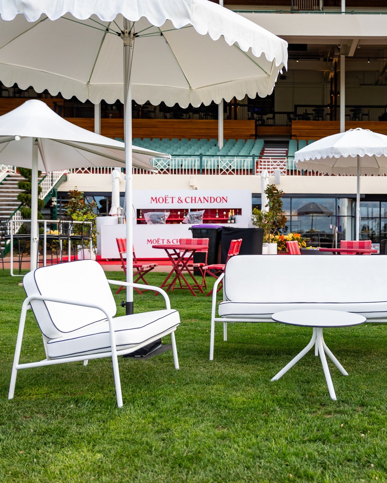 Outdoor setting with white chairs, tables, and umbrellas under a large tent with Moët & Chandon branding.