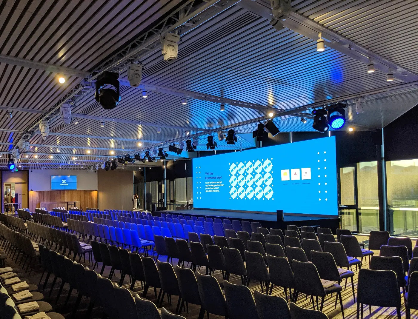 Conference hall set up with chairs facing a stage with a large LED screen
