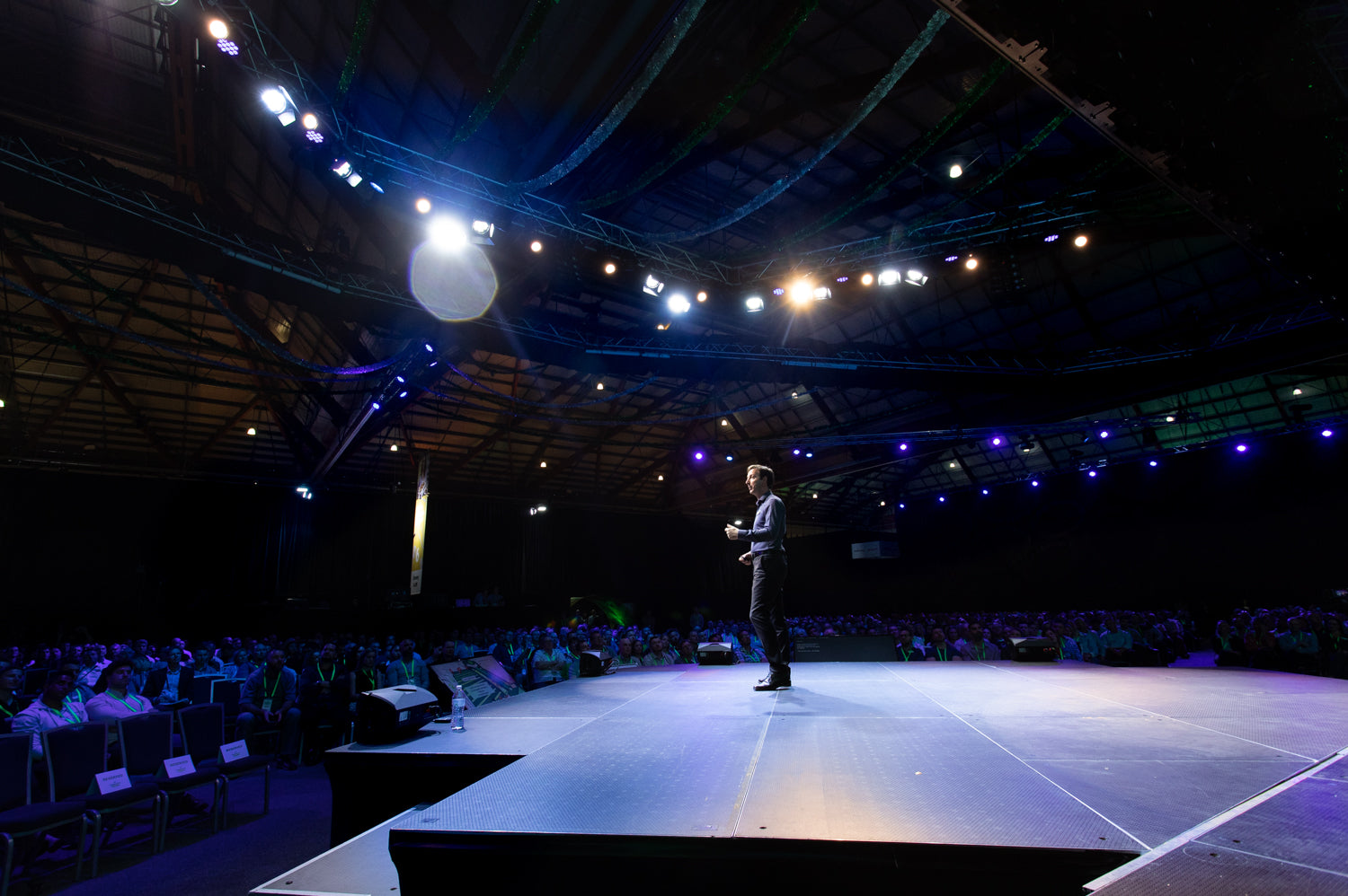 Person standing on a stage in a large auditorium with dim lighting