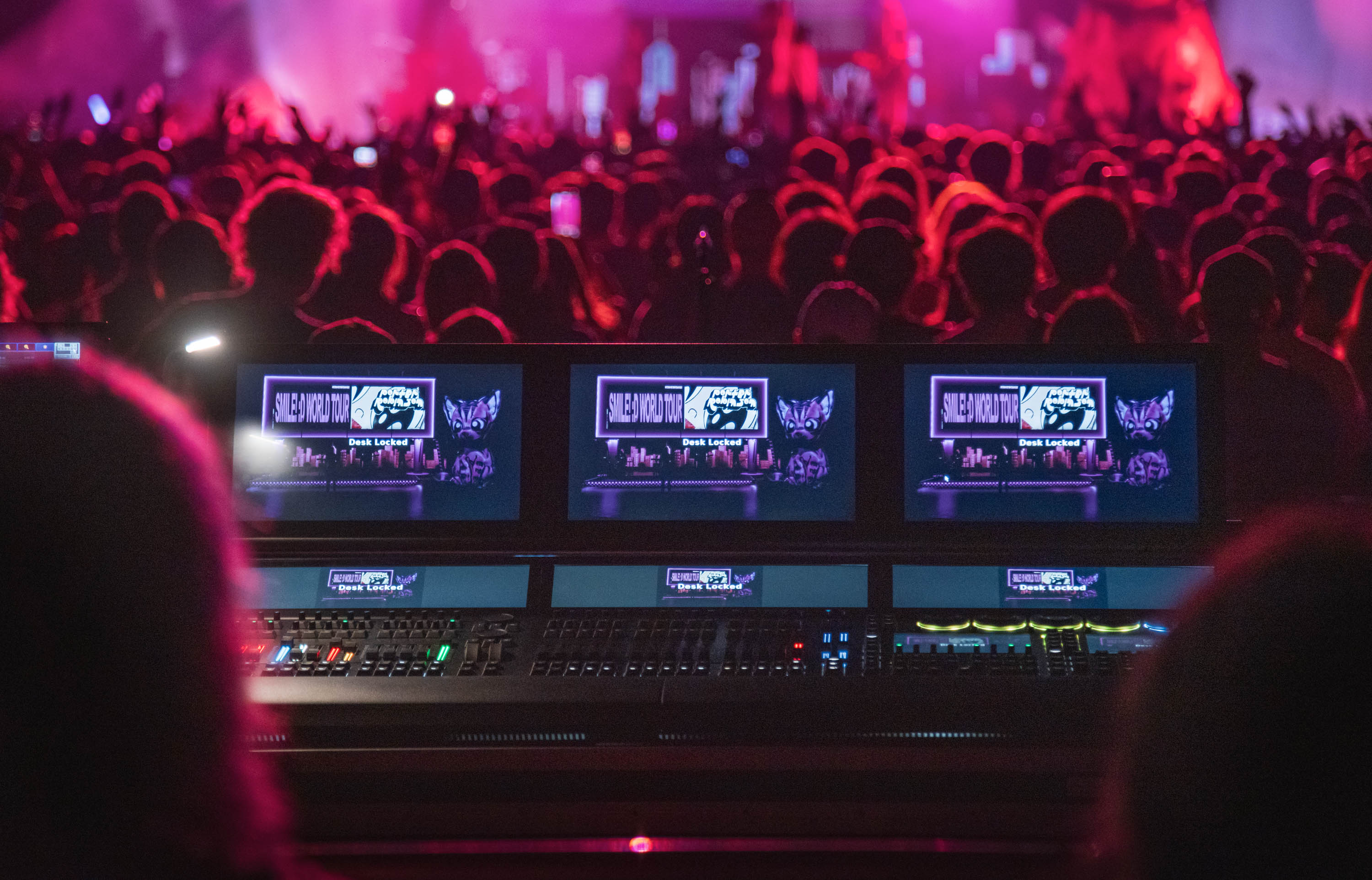 Control room with multiple monitors displaying a live event, with a crowd in the background.