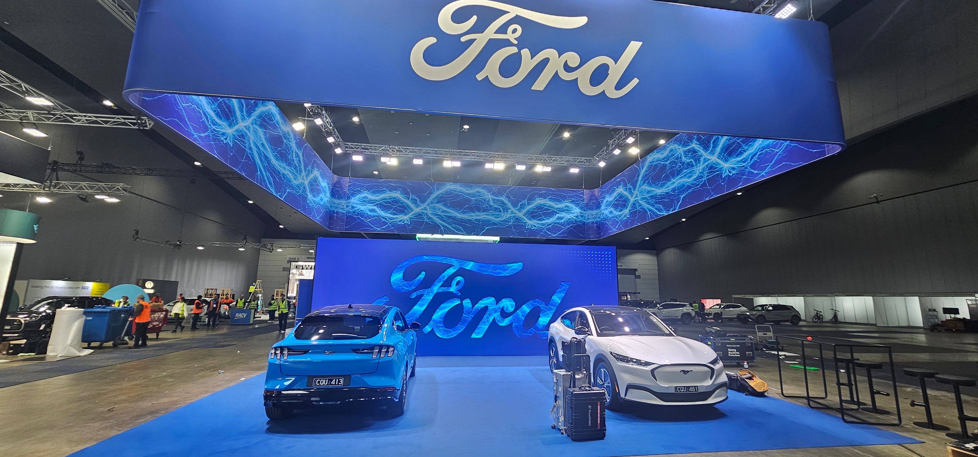Ford display with two cars underneath a large Ford sign at an indoor event.