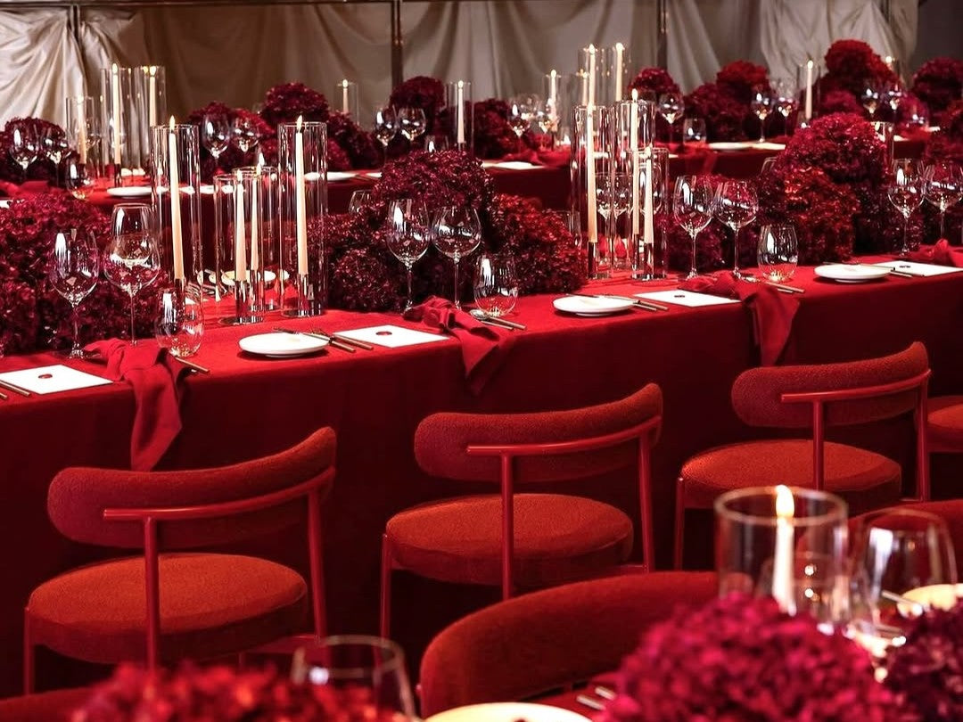 Decorative table setting with red tablecloths, candles, and wine glasses in a formal event setup. Featuring our Margot chairs