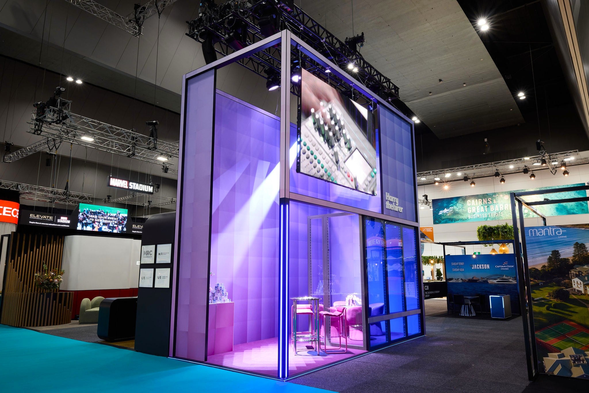 Exhibition booth with digital display and seating area in a convention center