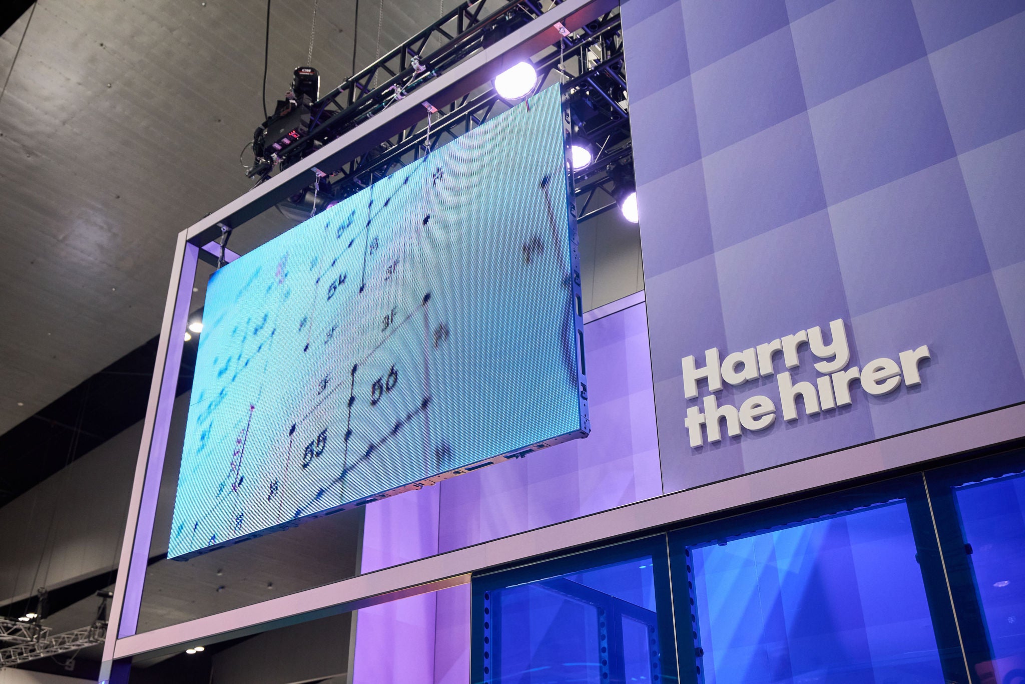 Large screen displaying a map with 'Harry the Hirer' branded expo stand on a purple background.