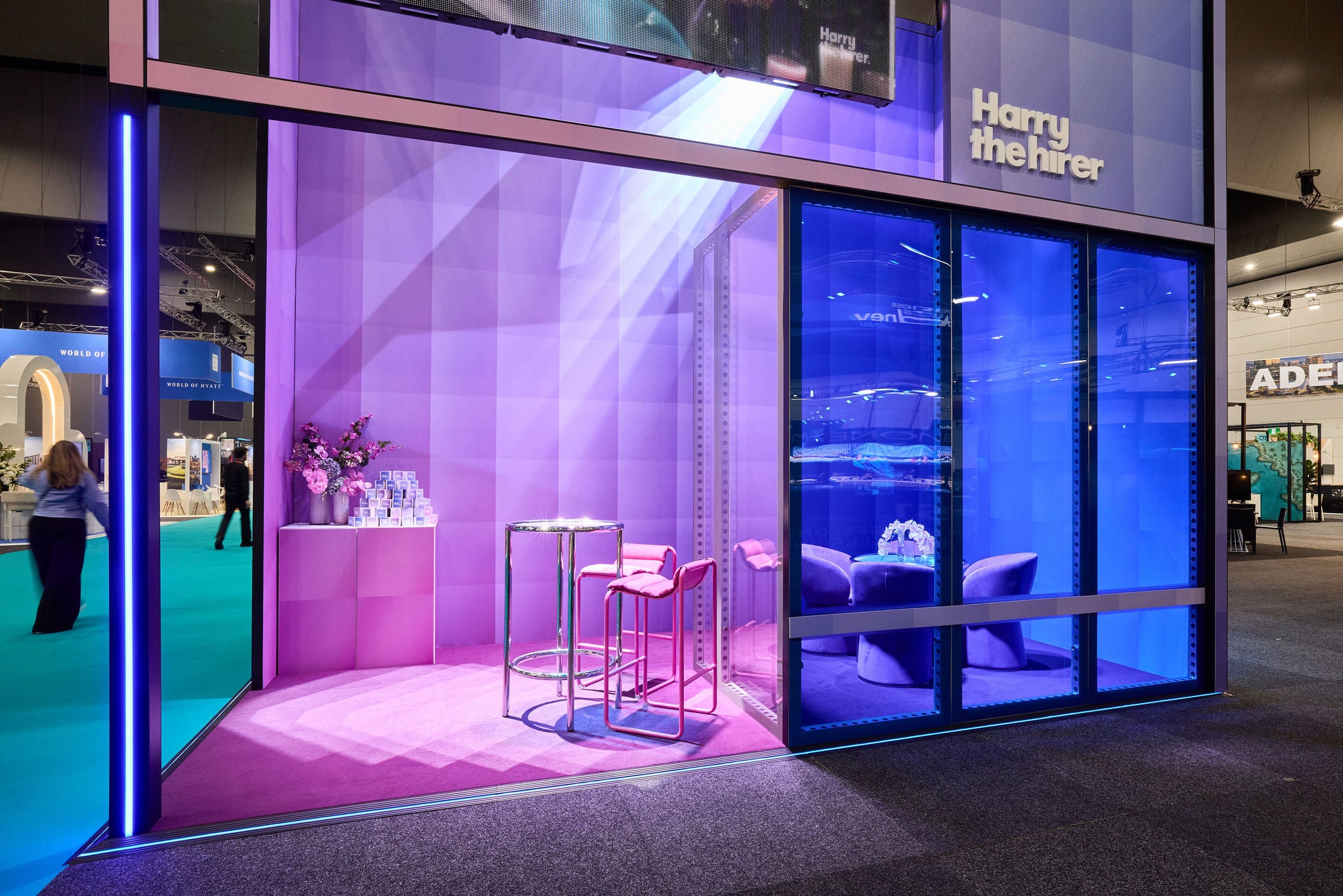 Exhibition stand with purple and blue lighting, featuring 'Harry the Hirer' branding.