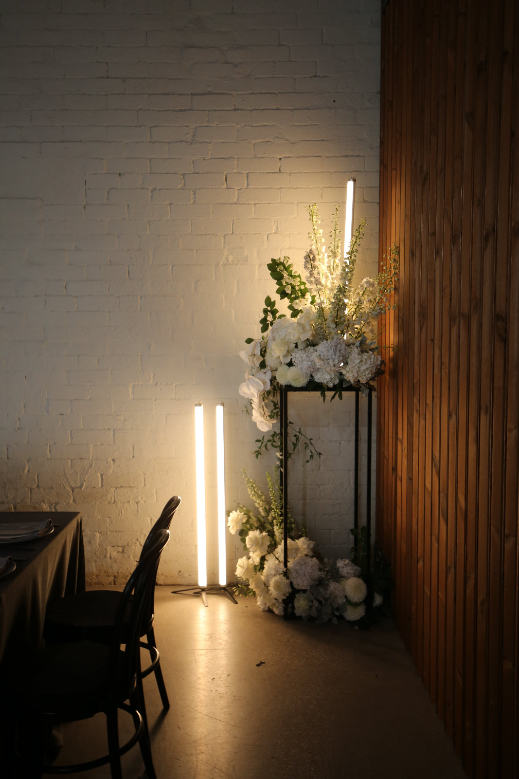 Floral arrangement with white flowers and greenery against a white brick wall.