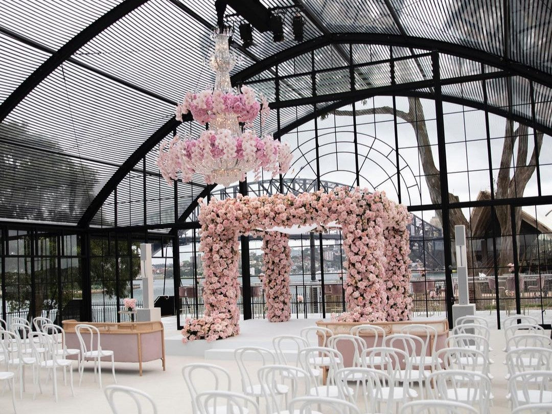 Decorative floral arch and chandelier in an Atrium Marquee with chairs and tables for a private wedding.