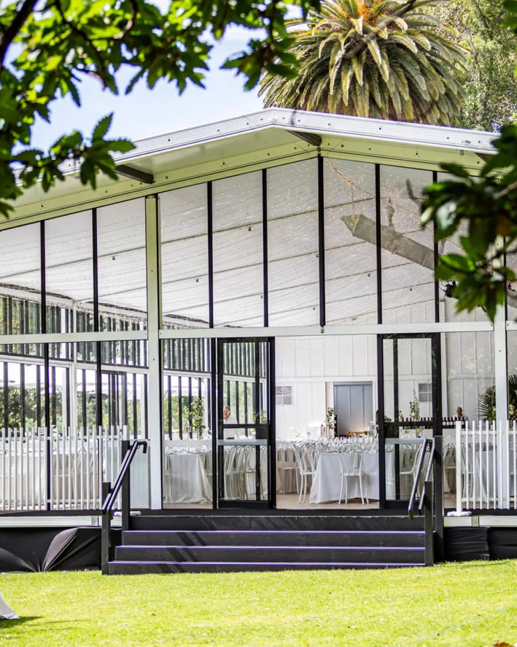 Modern building with large glass windows and white exterior, surrounded by greenery.