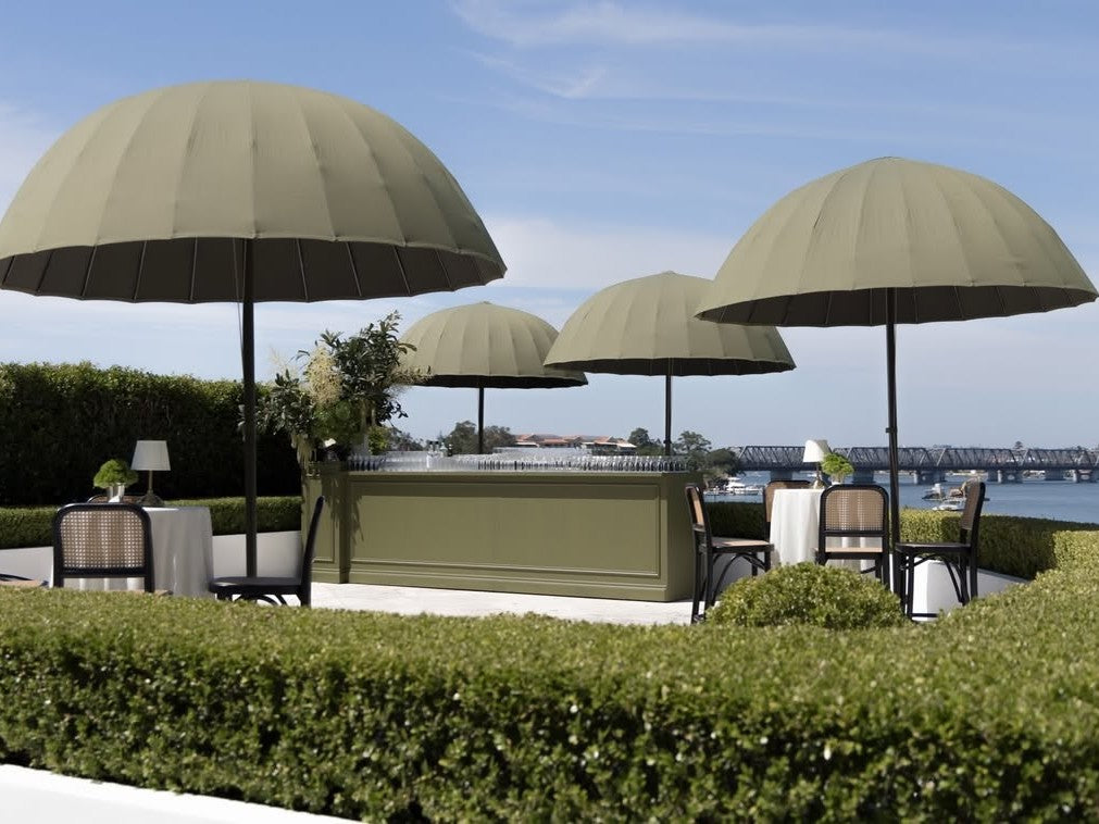Outdoor seating area with green Isla umbrellas and tables by a waterfront for a wedding